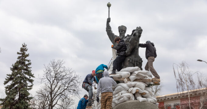 KYIV, UKRAINE – Mar. 26, 2022: War in Ukraine. Monument to Hetman Sahaidachny with sandbags to protect against Russian shelling in Kyiv. A group of young people cover the monument with sandbags